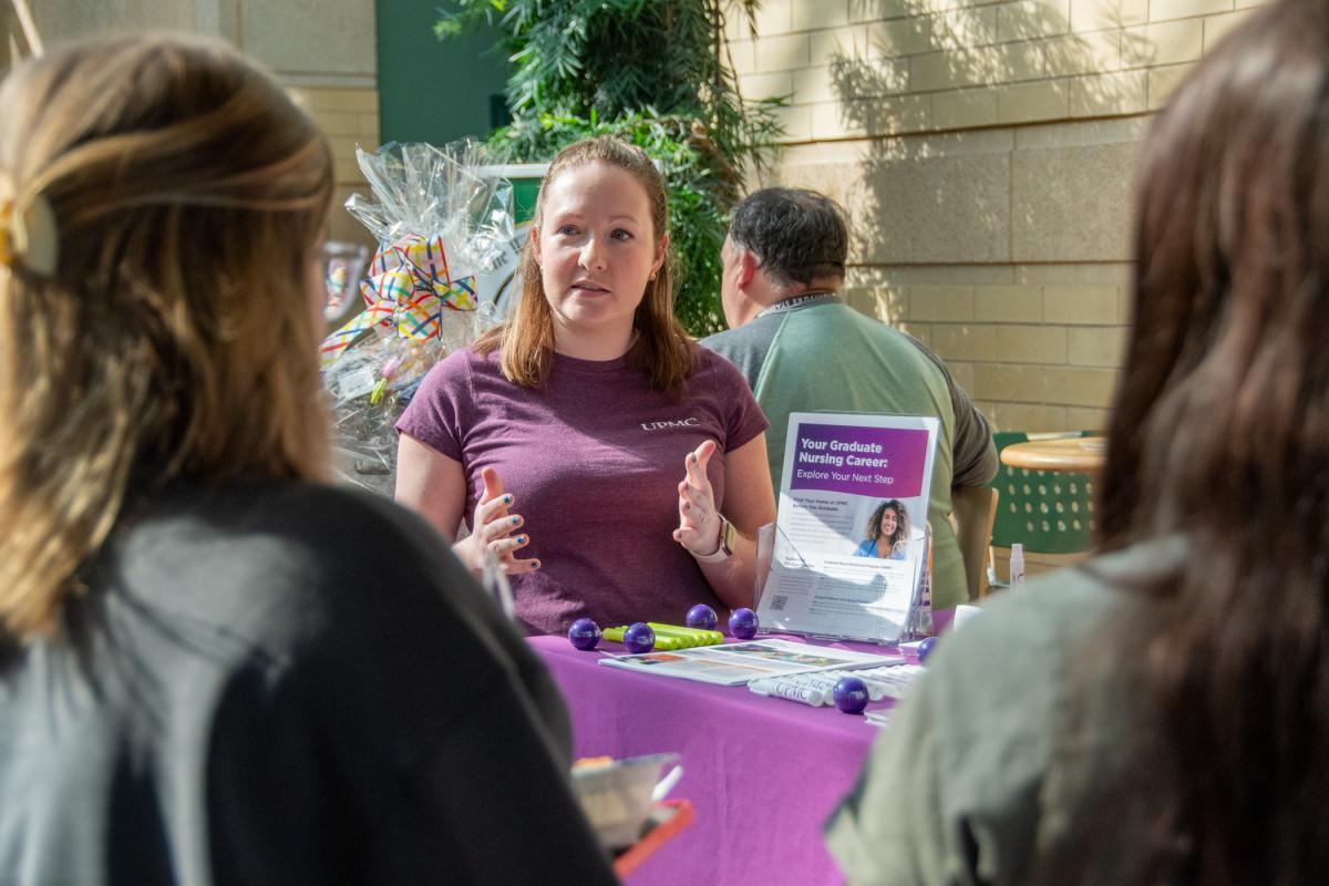 A UPMC representative meets with two student at a health services career fair.