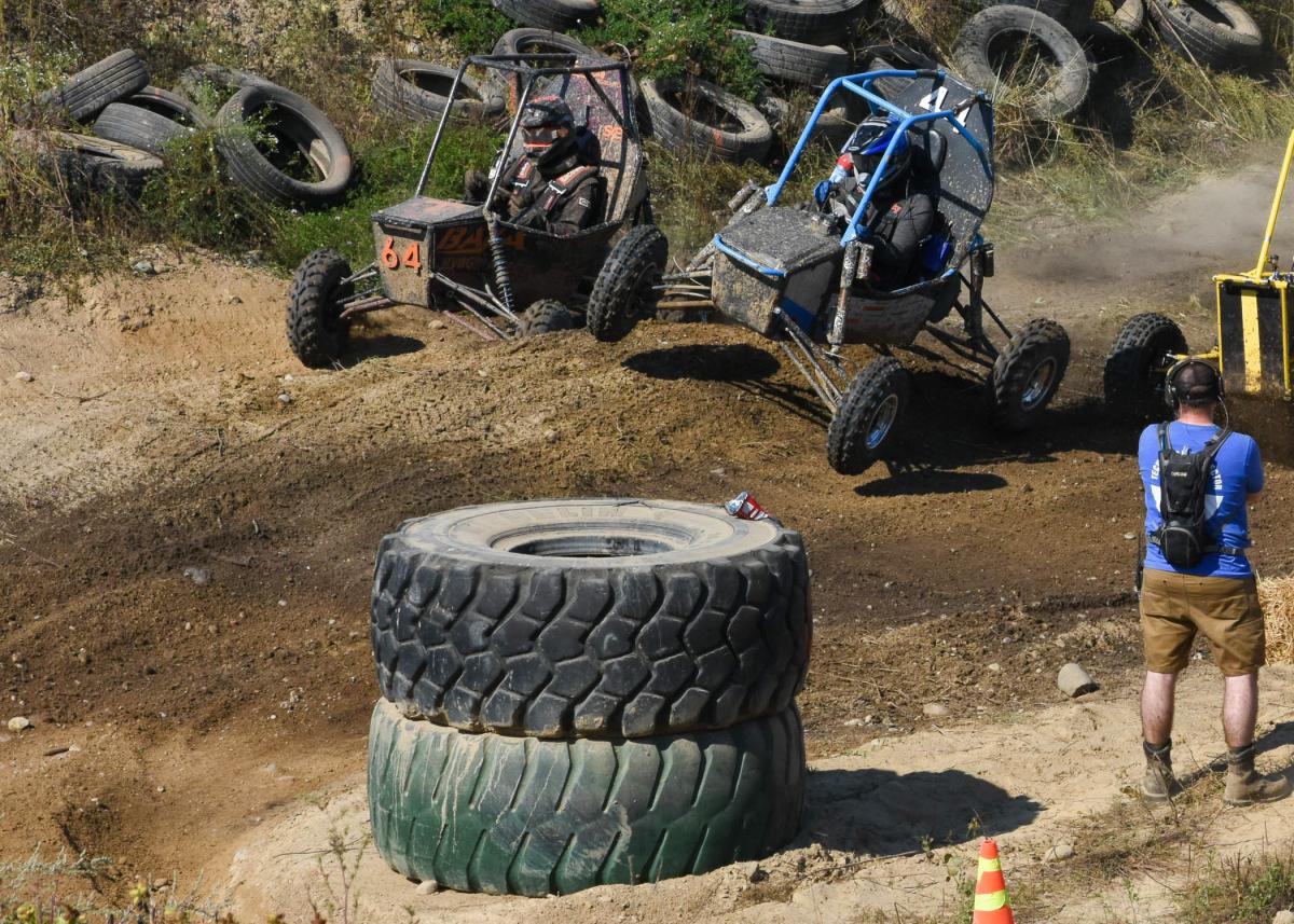 Two off-road Baja vehicles racing around a dirt turn, with a photographer nearby.