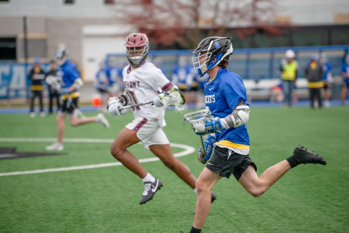 A Penn College lacrosse team member running against a competitor on the game field
