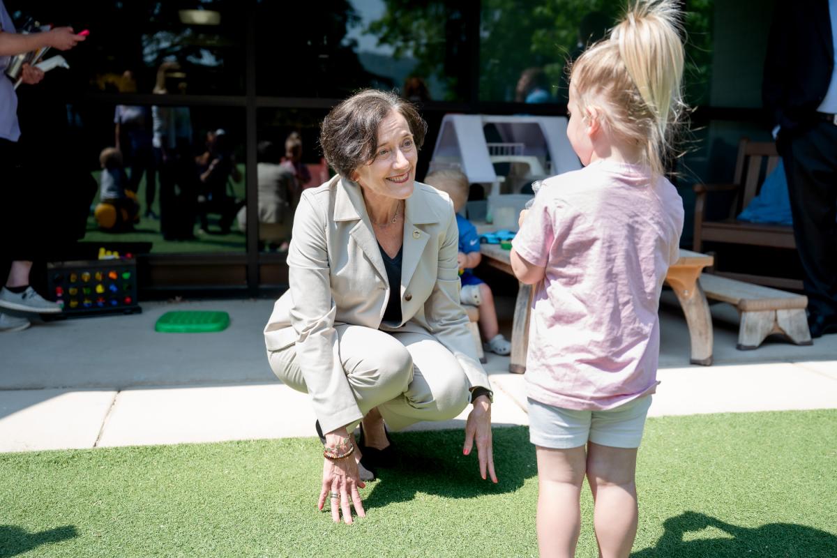Adult kneeling and talking with a young child outdoors during a group activity