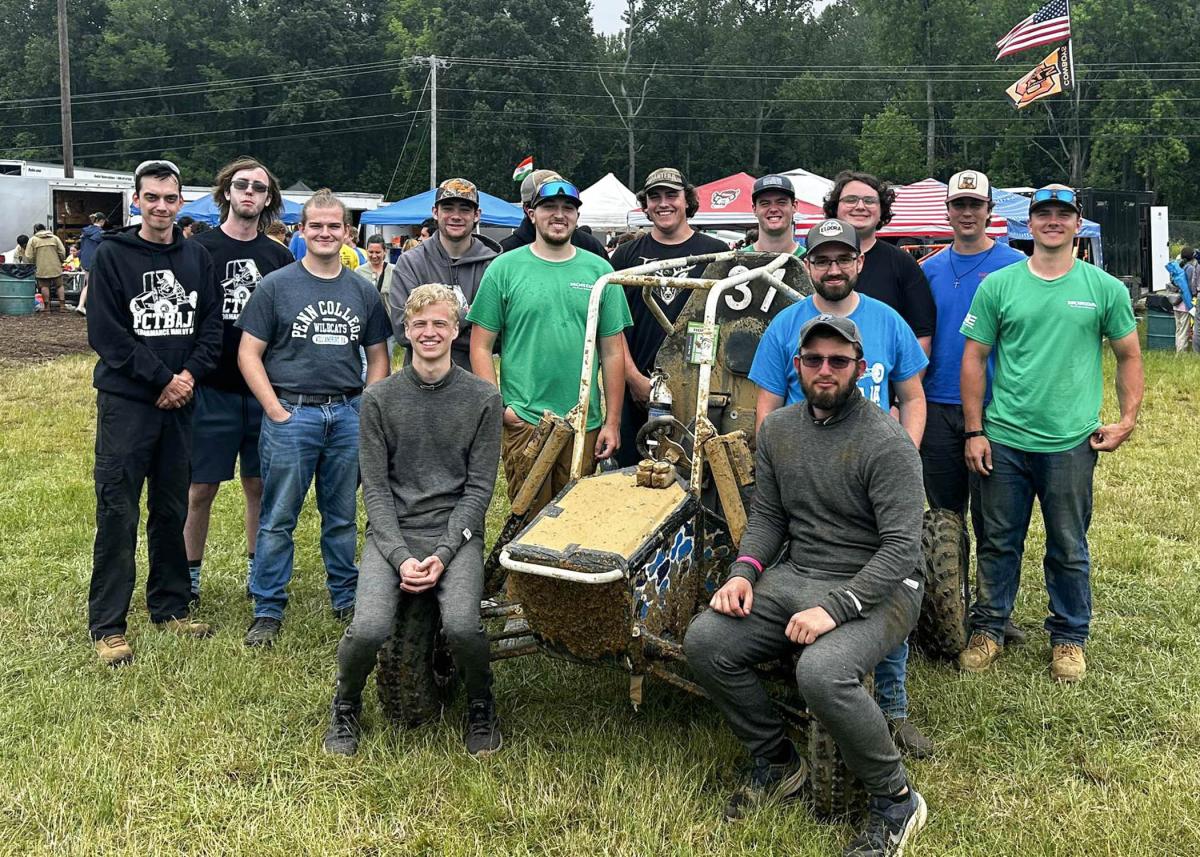 A group of Penn College students standing and sitting around a custom-built off-road vehicle at the Baja SAE competition.