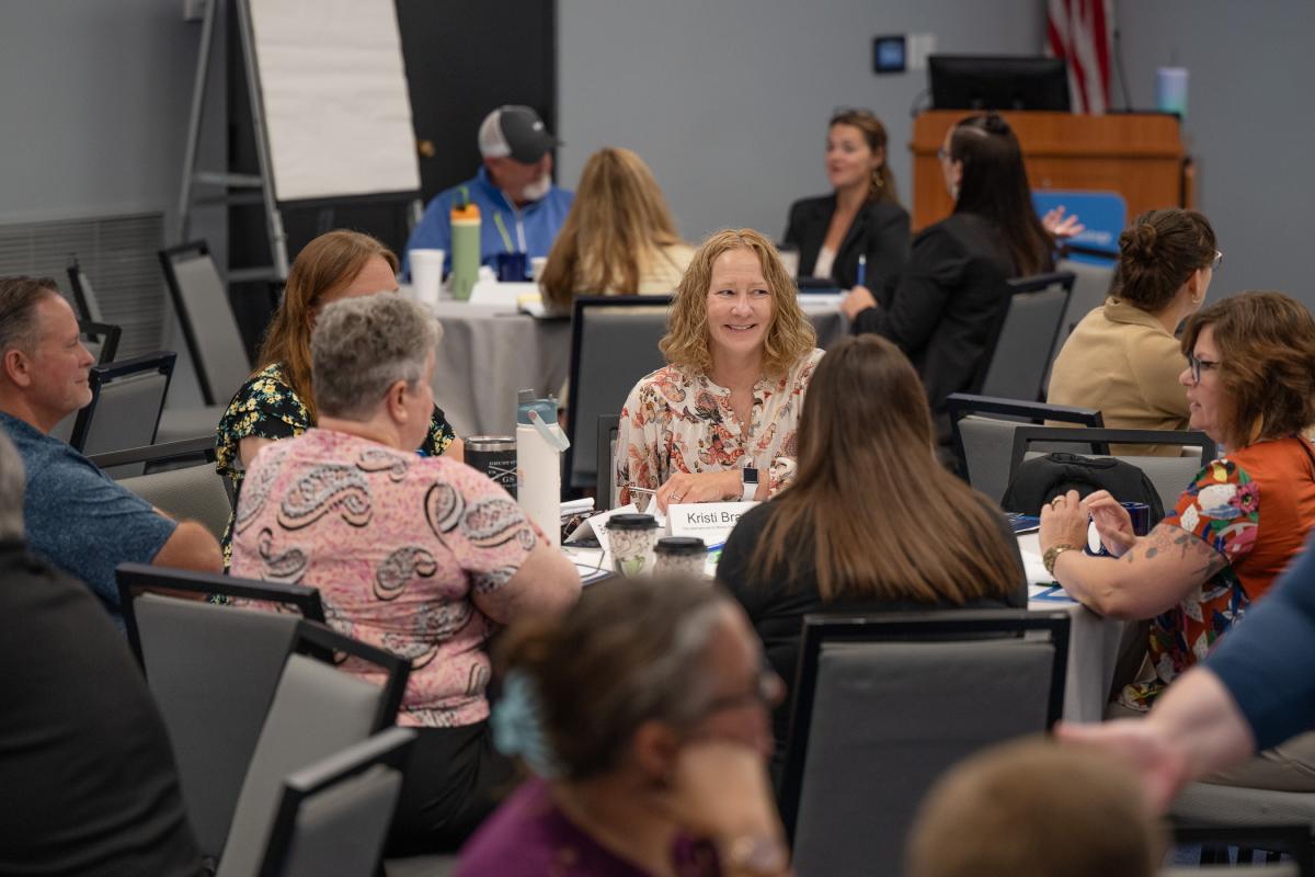 Attendees seated at large round tables participate in a large group training