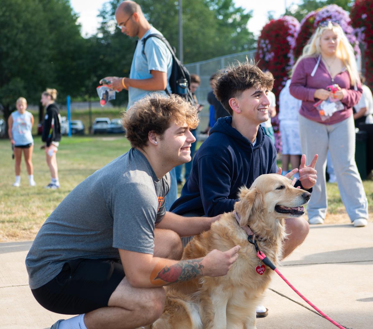 Two students pose for the camera with a golden retriever