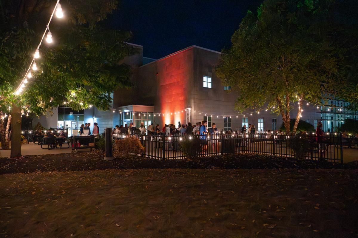 Students and alumni gather for an evening Welkwome Weekend events under lights on the Madigan Library patio.