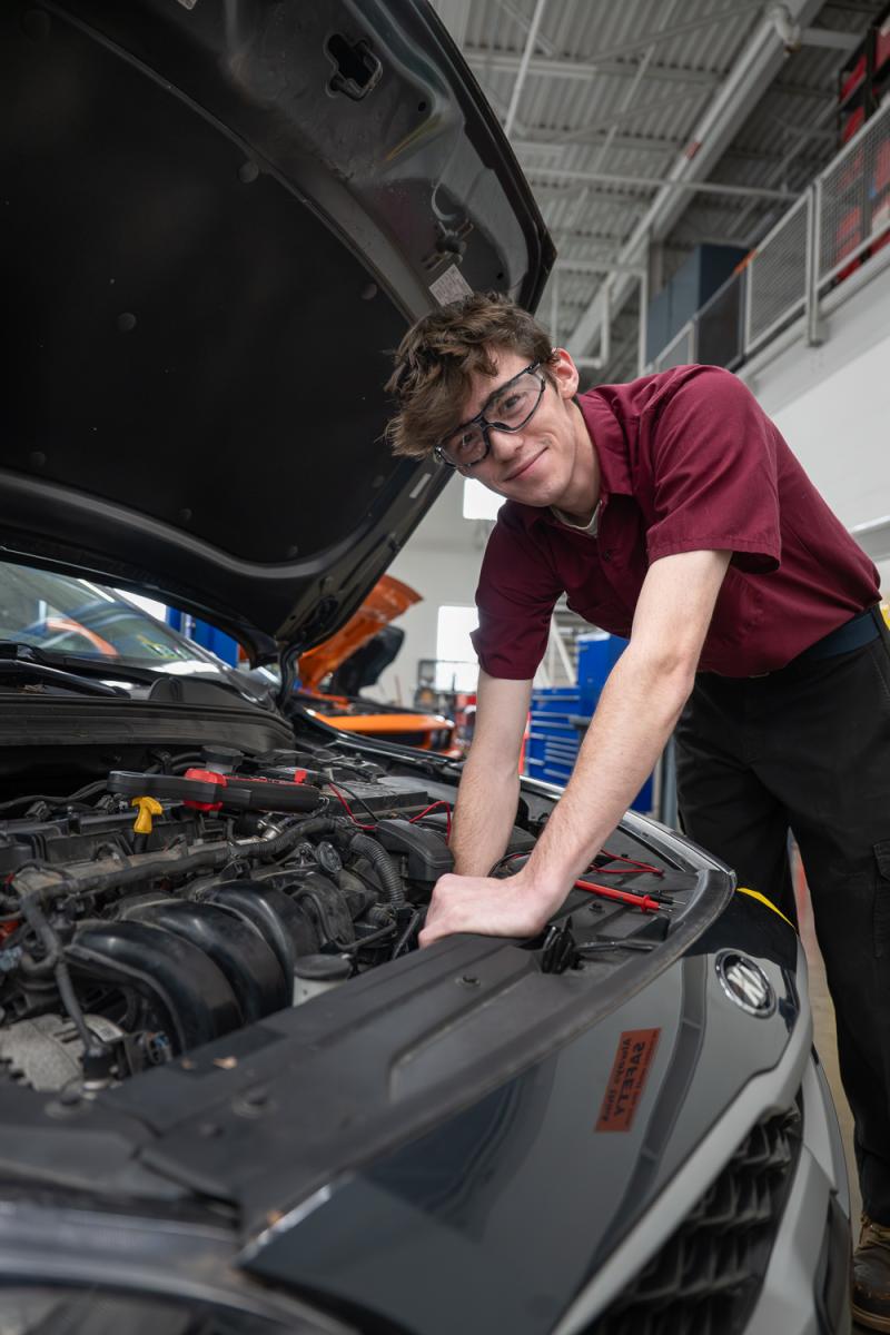 Person working under the hood of a car in an automotive workshop