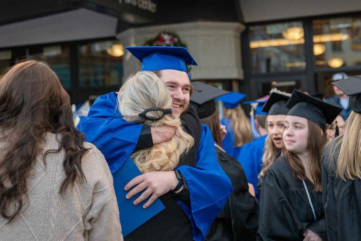 A graduate gives a hug outside the Community Arts Center among other graduates and guests.
