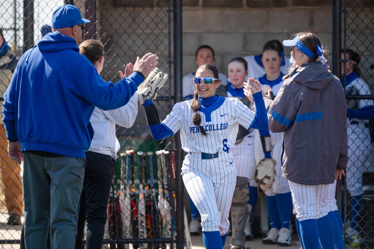 A softball player gives high fives as she runs out of the dugout.