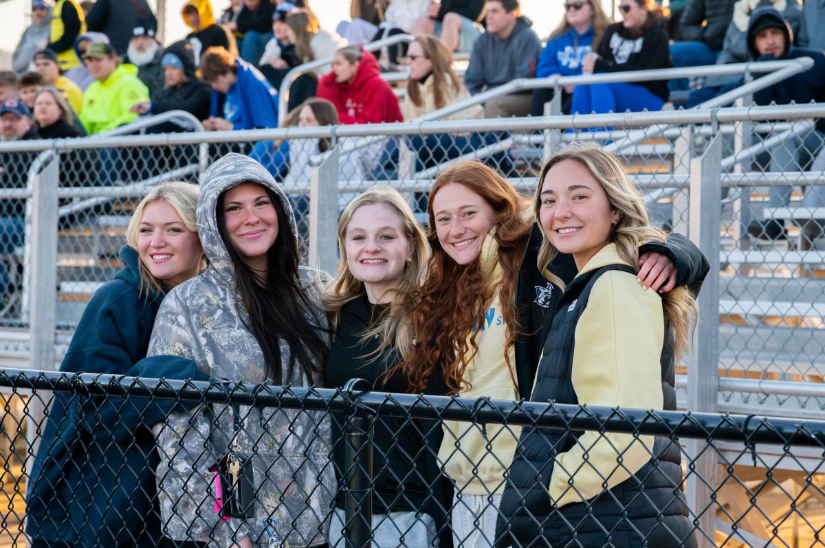 Group of spectators standing and posing by a fence at a sports stadium