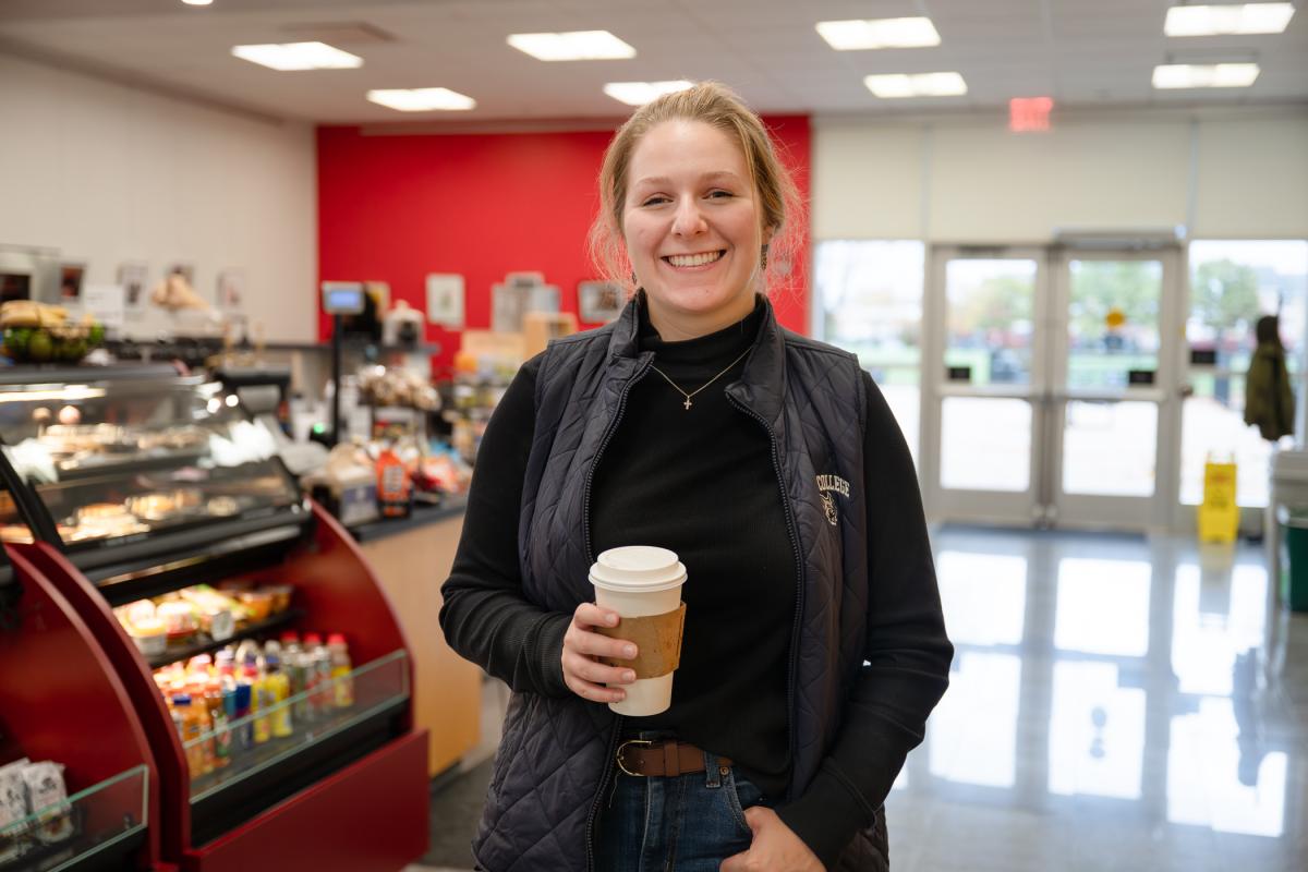 A student holding a to go cup with Bookmarks Cafe in the background
