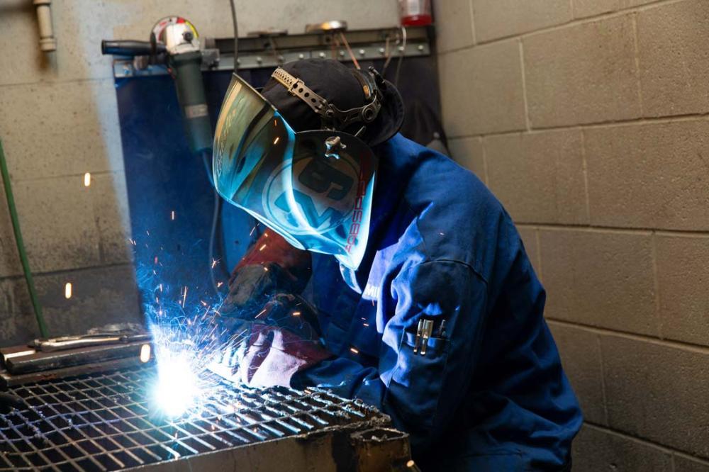 Person welding metal at a workbench, with sparks flying in a workshop.