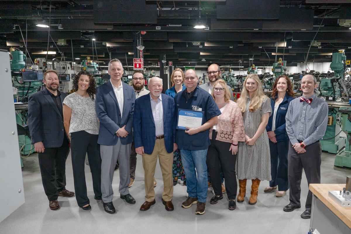 A large group of people poses inside Penn College's Larry A. Ward Machining Technologies Center.