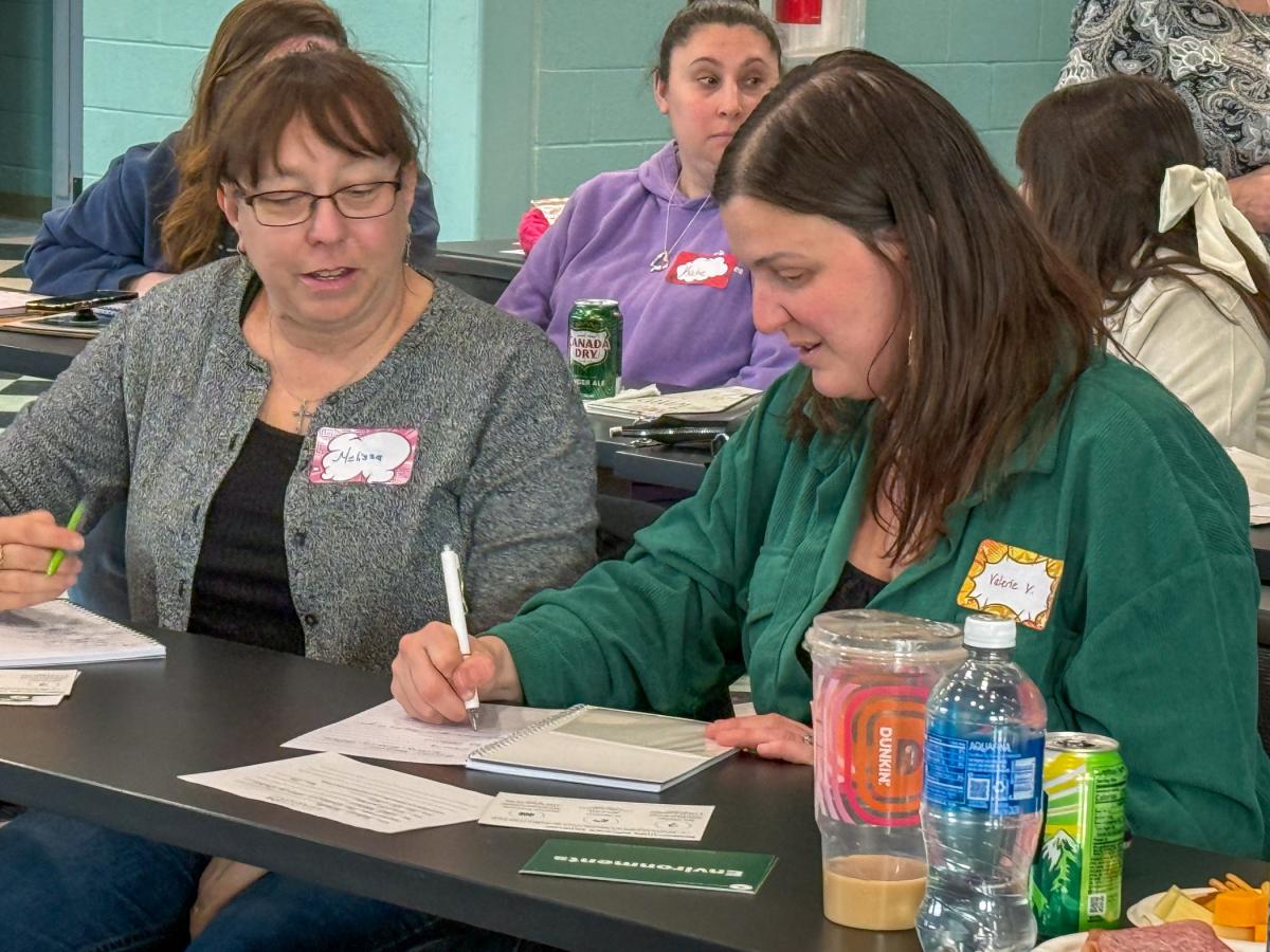 Adults sit at a table in a conference room taking notes.