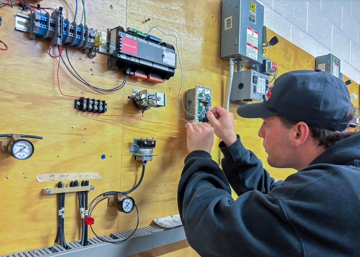 A student runs a control power wire to a thermostat in a Pennsylvania College of Technology building automation lab.