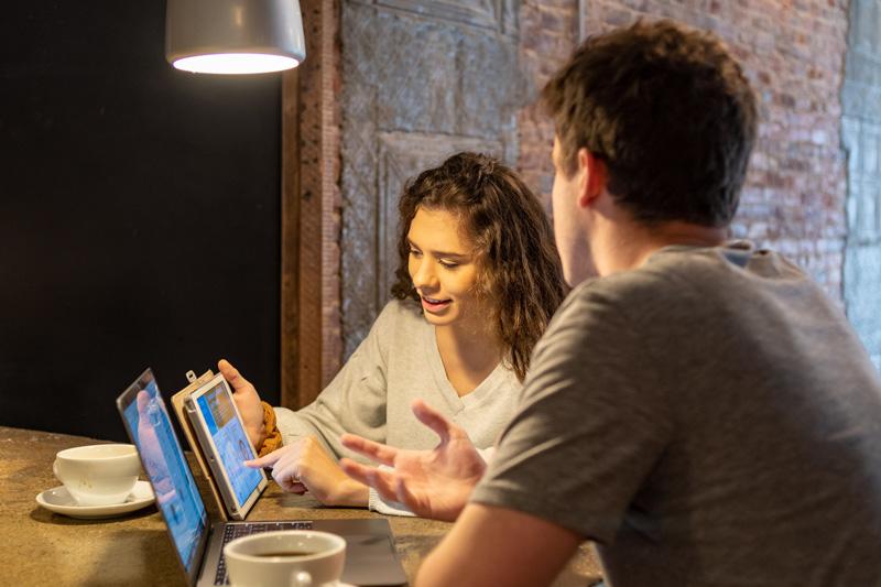 A young man and women in discussion at two laptops in a coffee shop