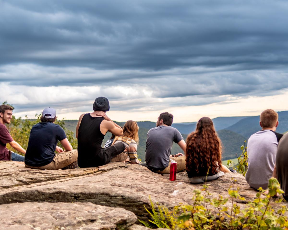 a group of students seated on a rock ledge overlooking a tree lined canyon and distant mountains
