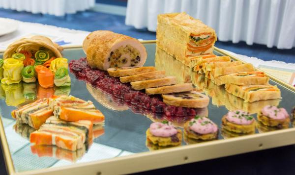 Assortment of gourmet appetizers and sliced entrées displayed on a mirrored tray.