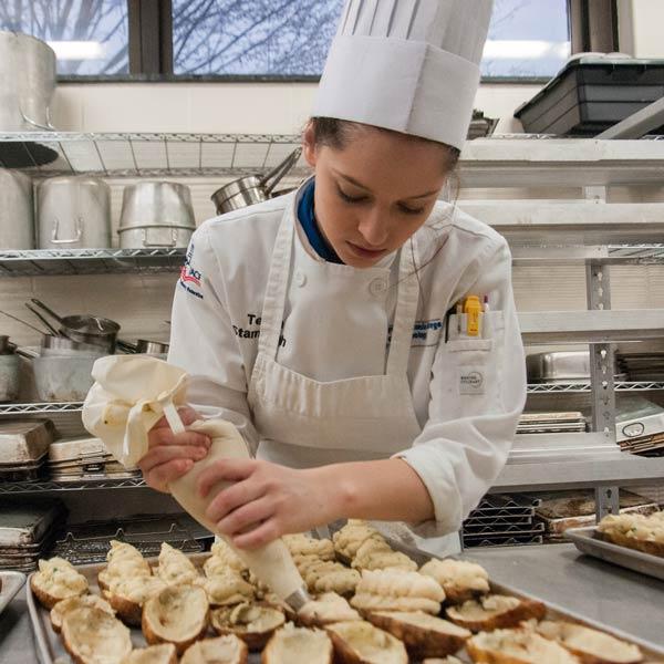 A Penn College Culinary Applications student prepares food in a hands‑on kitchen lab, building foundational culinary skills.