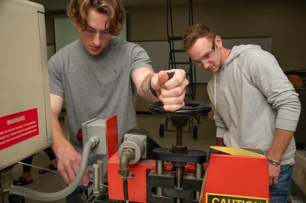 Two students work on a piece of plastics extrusion equipment.