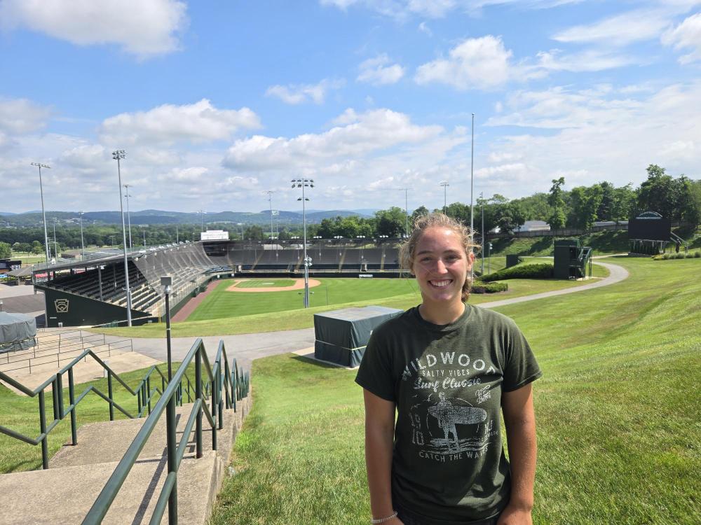 Trinity Willoughby stands on a hill with Lamade Stadium, site of the Little League Baseball World Series, in the background.