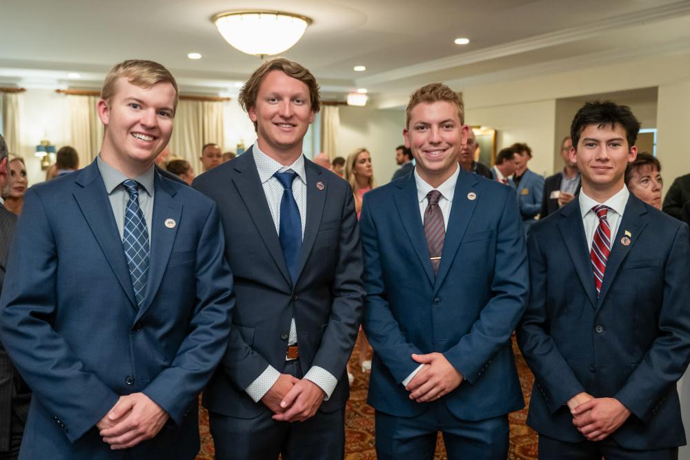 Four students in suits and ties smile at the camera.