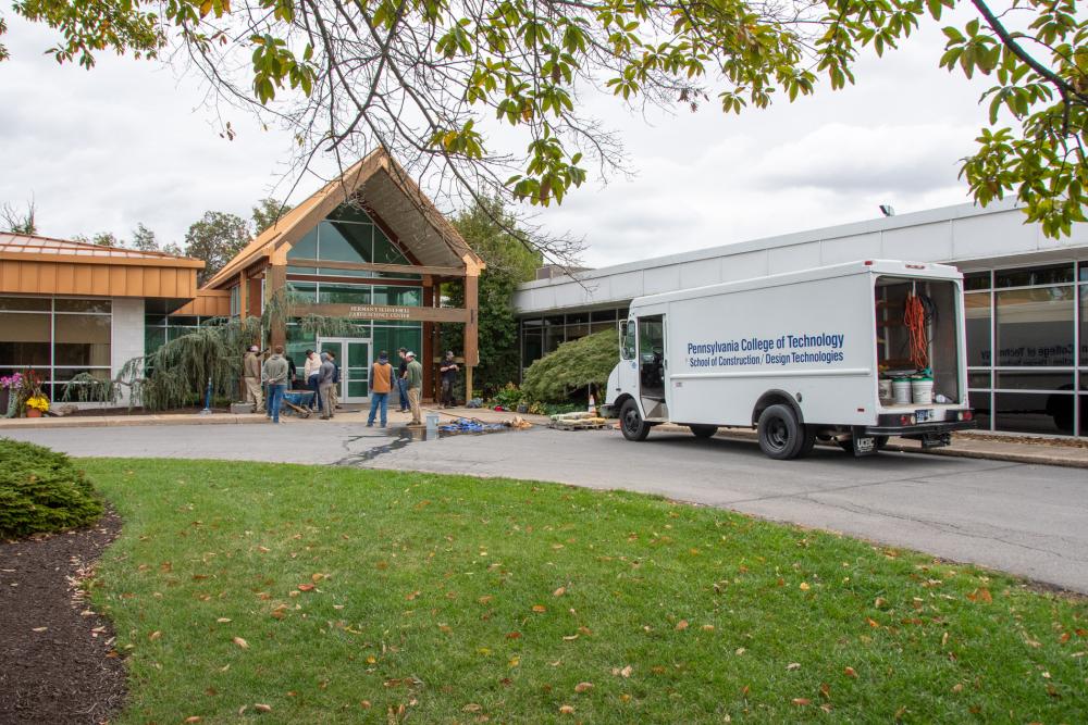 A Pennsylvania College of Technology Construction/Design Technologies truck sits in front of the Scheebeli Earth Science Center while masonry students work at the building's entrance.