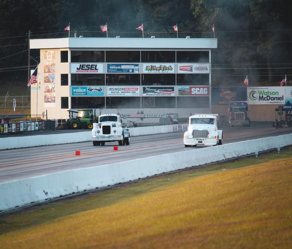 Two tractor trailer trucks race down a track.