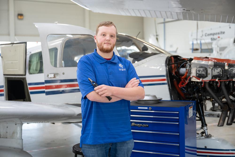 A student stands with arms crossed in front of an airplane and large toolbox.