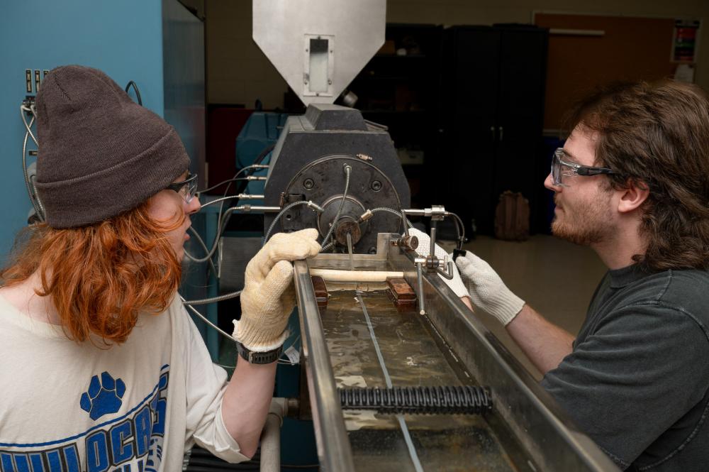 Two students interact with a plastics extrusion machine.