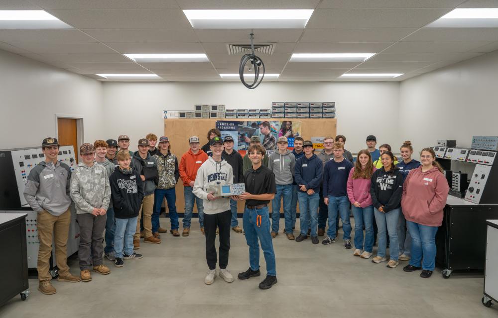 A group of students from Miffling County Aacademy of Science and Technology stands in a Penn College electrical lab. Two in the center are holding a piece of electrical equipment.