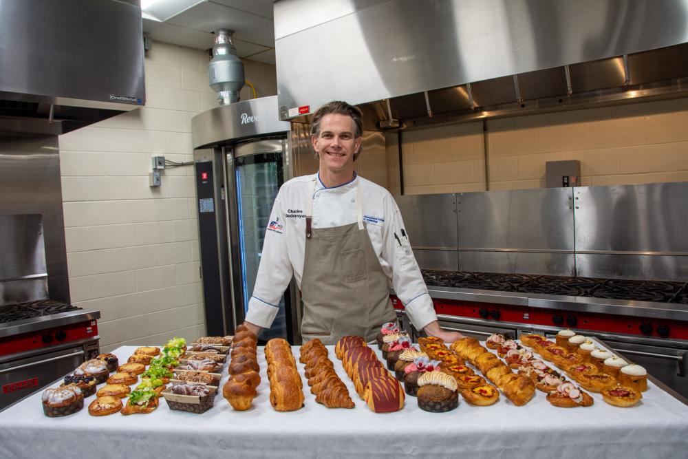Chef Charles Niedermyer stands behind a table of laminated pastries in a Penn College baking lab.