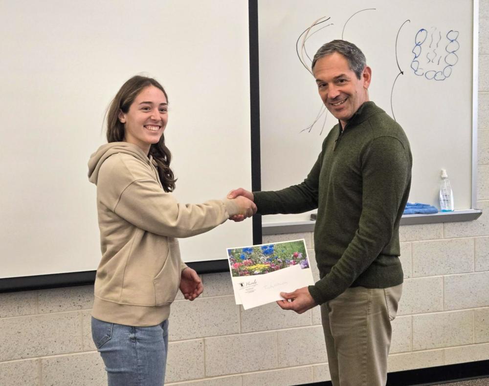 Two people shake hands. One is handing papers to the other.