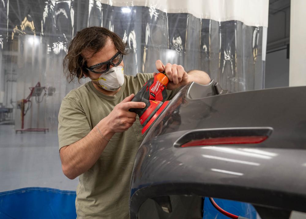 A Penn College student applies a Milwaukee random orbital sander to a vehicle bumper.
