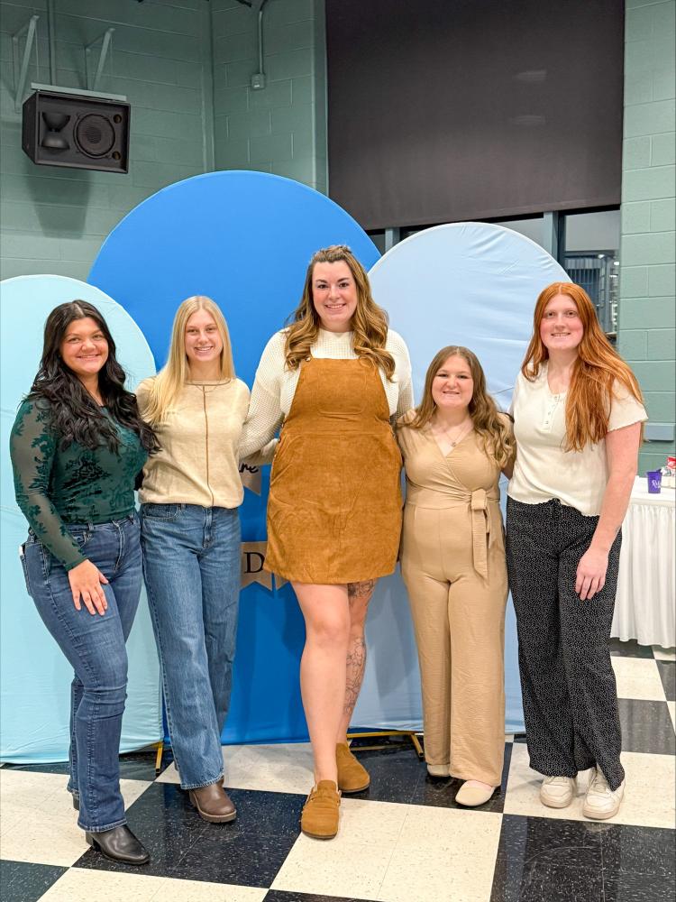 Five nursing students stand arm-in-arm against a blue backdrop in Penn College's Penn's Inn.