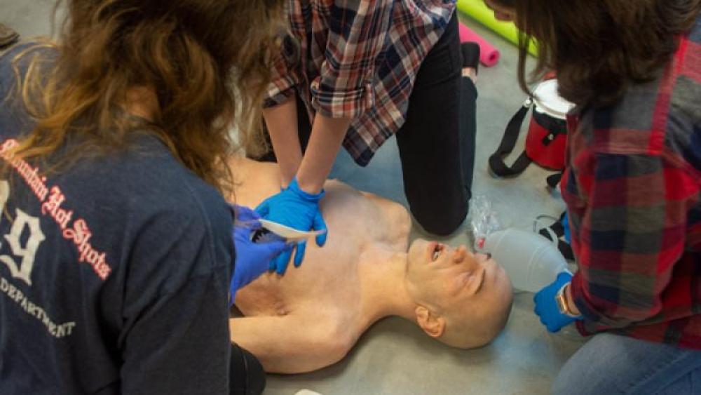 Students practice chest compressions and breaths on a mannequin.