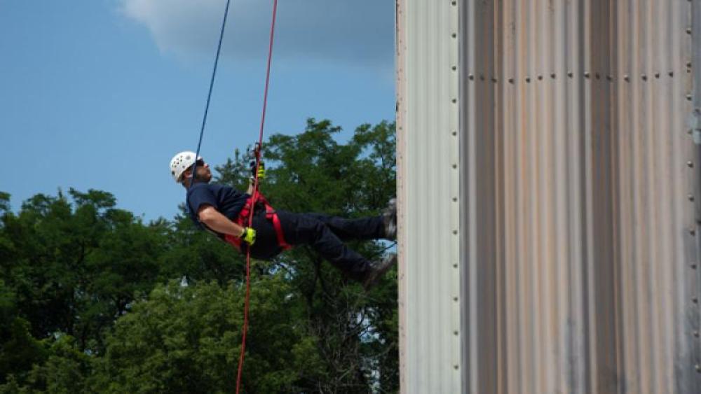 A person on a repel line climbs a metal wall