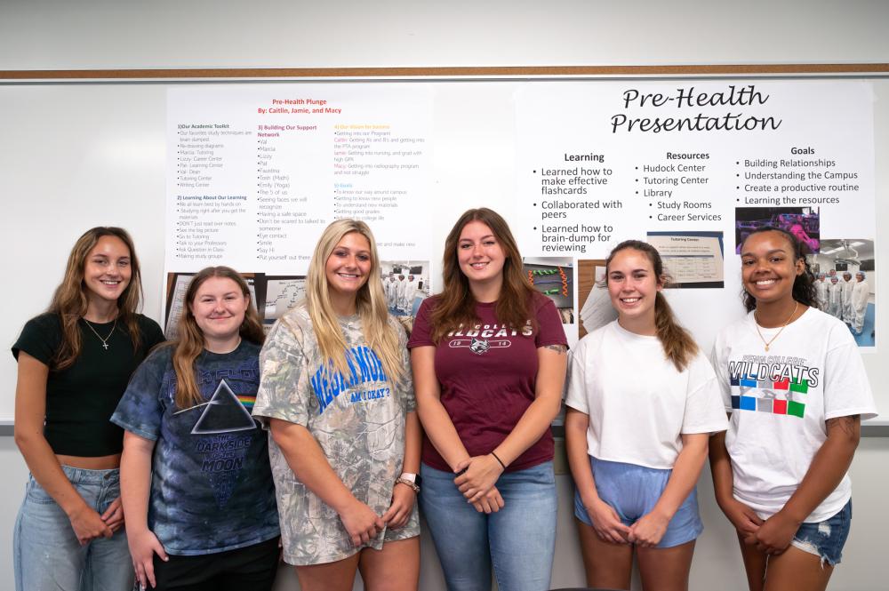 Group of students standing in front of a pre-health presentation poster in a classroom