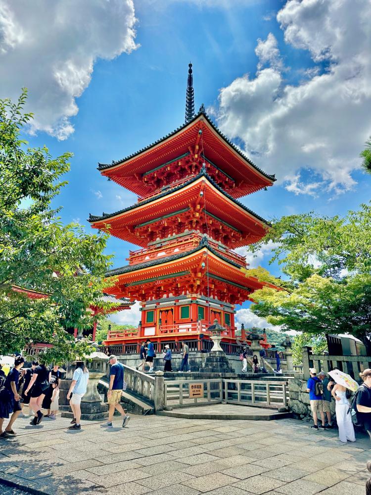 Red multi-tiered pagoda surrounded by trees with visitors walking nearby