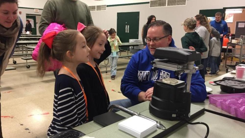 A Plastics Mobile Lab facilitator speaks with two girls at a workstation