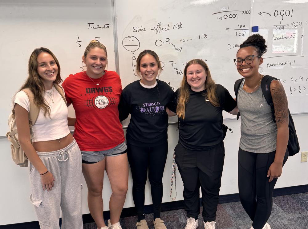 students pose in front of a whiteboard with formulas