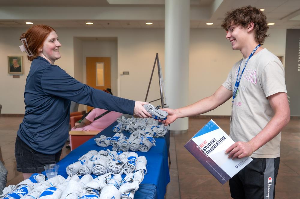 Student handing new student orientation folder and tshirt