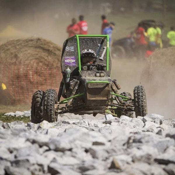 Off-road race vehicle driving over rocks during a dusty course event.