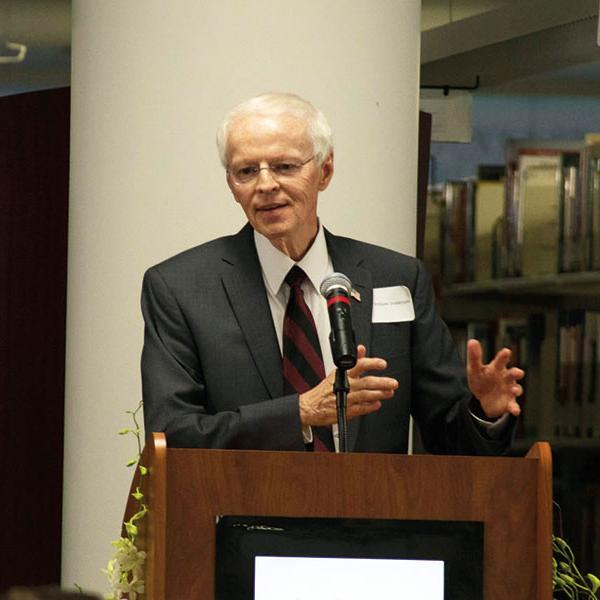 William Feddersen, with gray hair and dressed in a suit, speaks from behind a podium.