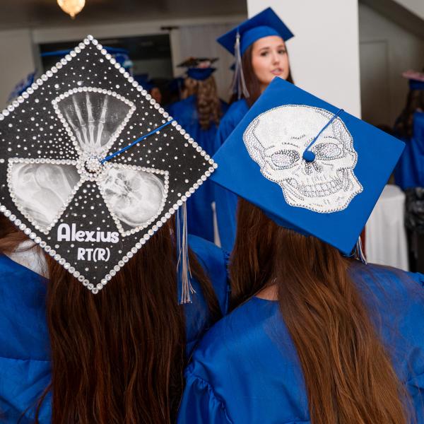 The backs of the heads of two Penn College radiography graduates, showing their decorated caps: One with X-ray images, the other with a skull.