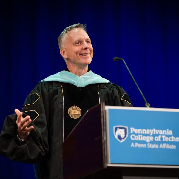 Penn College President Michael J. Reed stands behind a podium, using his hands while he speaks and smiles.