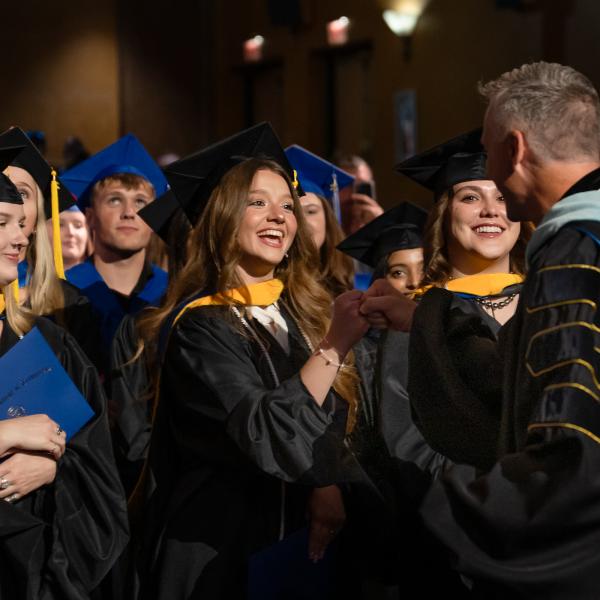 Penn College President Michael J. Reed fist bumps smiling graduates in their seats at the Journey Bank Community Arts Center.