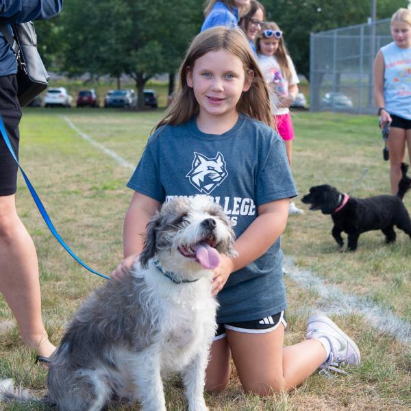 A child kneels next to a gray-and-white dog.