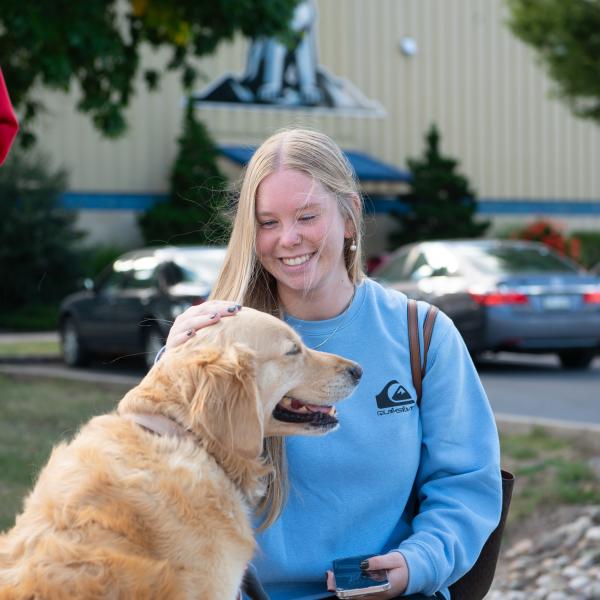 A student smiles while petting a dog.