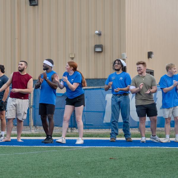 Students in blue shirts cheer from the sidelines.