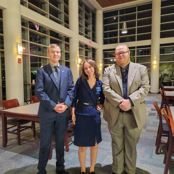 Three people in business attire stand in front of floor-to-ceiling windows in Penn College's Madigan Library.