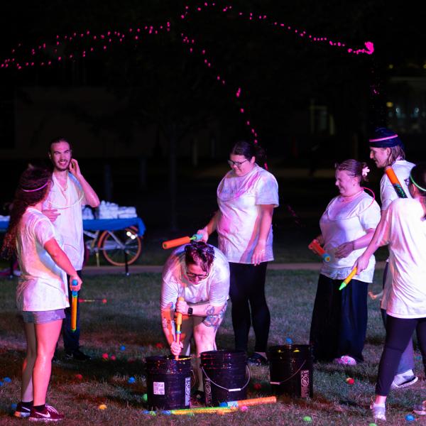 Glowing pink paint splatters float through the air above the heads of several smiling students.